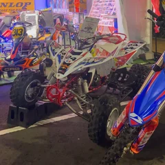 A white and red quad displayed among karts and motorcycles at Bagatelle Motor Festival at night.