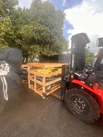 A forklift handling a wooden crate containing a yellow quad outdoors.