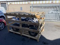 A white and black quad secured inside a timber crate in a paved yard.