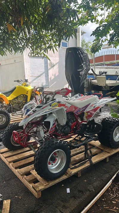 A white and red Yamaha quad secured with straps on a wooden pallet, with a yellow quad behind it.