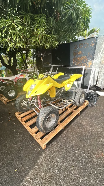 A yellow quad on a wooden pallet with its outer crate removed, beside loose packing material.