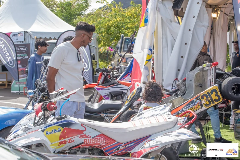 A person in a white shirt beside a child seated in displayed kart 313, among festival vehicles.