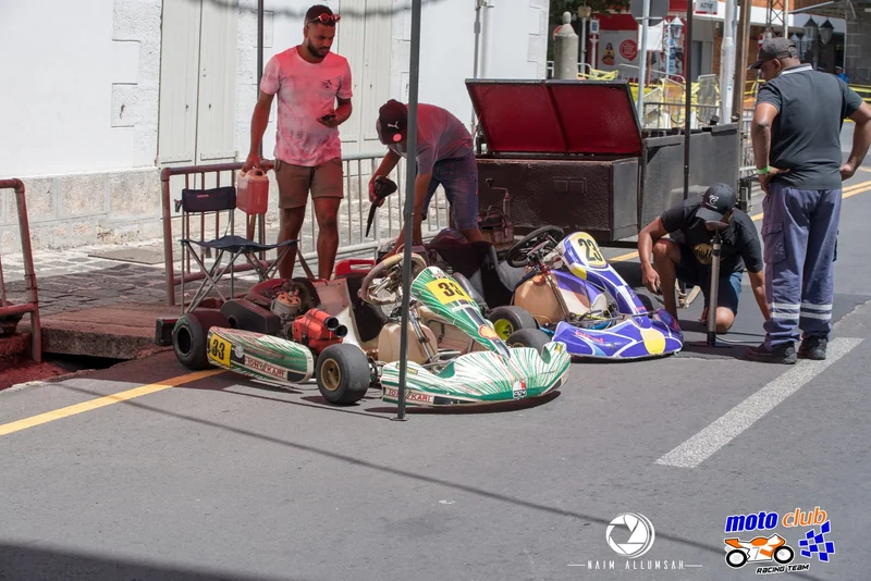 Drivers and supporting people preparing karts beside a city pavement.