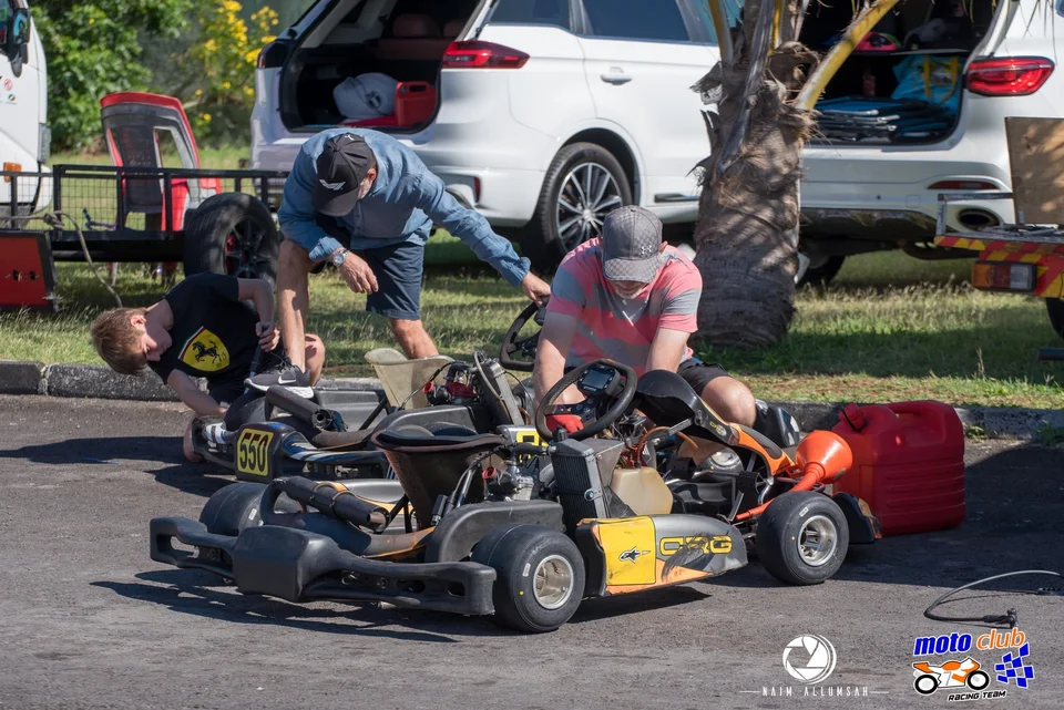 Three people preparing kart 550 and another kart in the paddock.