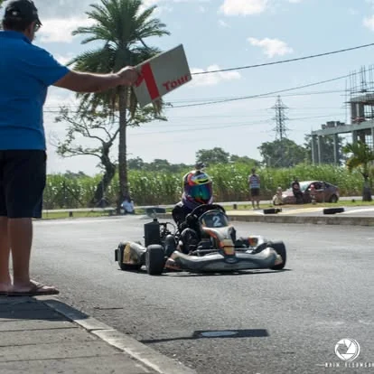 A person in blue holds a one-lap board as kart 2 approaches on the outdoor course.