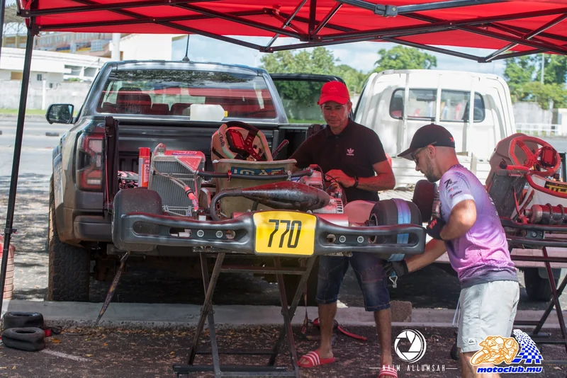 Two people working around kart 770 on a stand, beneath a red paddock canopy.