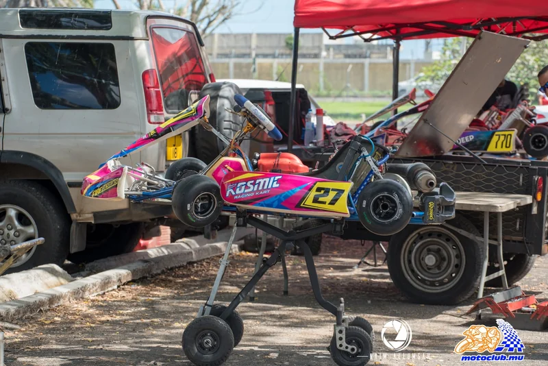 Kart 27 raised on a wheeled trolley beside a vehicle and other paddock equipment.